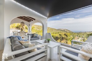 Een moderne buitenruimte met witte meubels, een tafel en uitzicht op een bergachtig landschap.