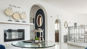 A modern living room with a glass coffee table, white sofas, a fireplace, and decorative wall art. - Villa INFINIDAD by Abahana Villas (Moraira)
