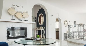 A modern living room with a glass coffee table, white sofas, a fireplace, and decorative wall art.