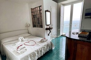 A hotel room with a bed, a small table, a mirror, and a view of the sea through the windows. - 2 Bed Flat - Sleeps 4 - Parking - Wifi (Ravello)