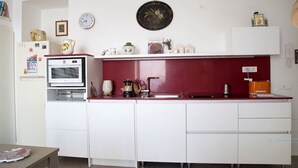 A compact kitchen with white cabinets, a red backsplash, and a microwave. There are various kitchen items on the countertop, including a coffee maker and a kettle. - 2 Bed Flat - Sleeps 4 - Parking - Wifi (Ravello)