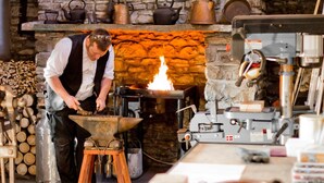 A blacksmith at work with a forge, anvil, and various tools.