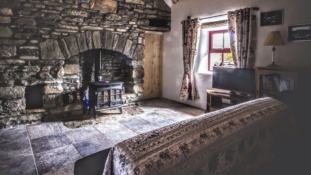 A cozy room with a stone fireplace, a wooden ceiling, and a window with curtains.