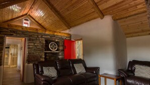 A cozy living room with a stone fireplace, leather sofas, and a wooden ceiling.