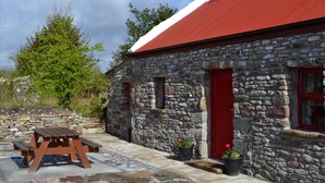 A stone building with a red roof, a wooden picnic table, and potted plants.