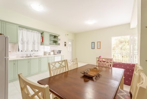 Un coin repas avec une table et des chaises en bois, une cuisine avec des meubles de couleur vert clair et une fenêtre donnant sur un paysage verdoyant.