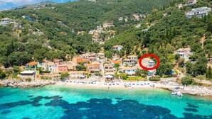 Uma vila costeira com edifícios numa encosta, uma praia com guarda-sóis e águas turquesa cristalinas.