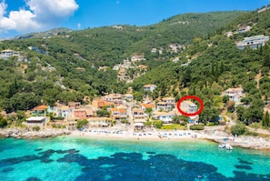 Une ville côtière avec des bâtiments construits sur une colline, une plage parsemée de parasols et une eau turquoise cristalline.