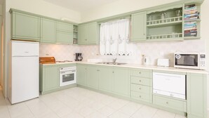 Uma cozinha com armários verdes, geladeira branca, fogão, micro-ondas e lava-louças.