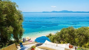 Uma piscina com água azul cristalina, rodeada por espreguiçadeiras e guarda-sóis, com vista para o mar e montanhas ao longe.