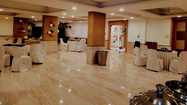 A spacious hall with white chairs and tables, a stage, and a large pillar.