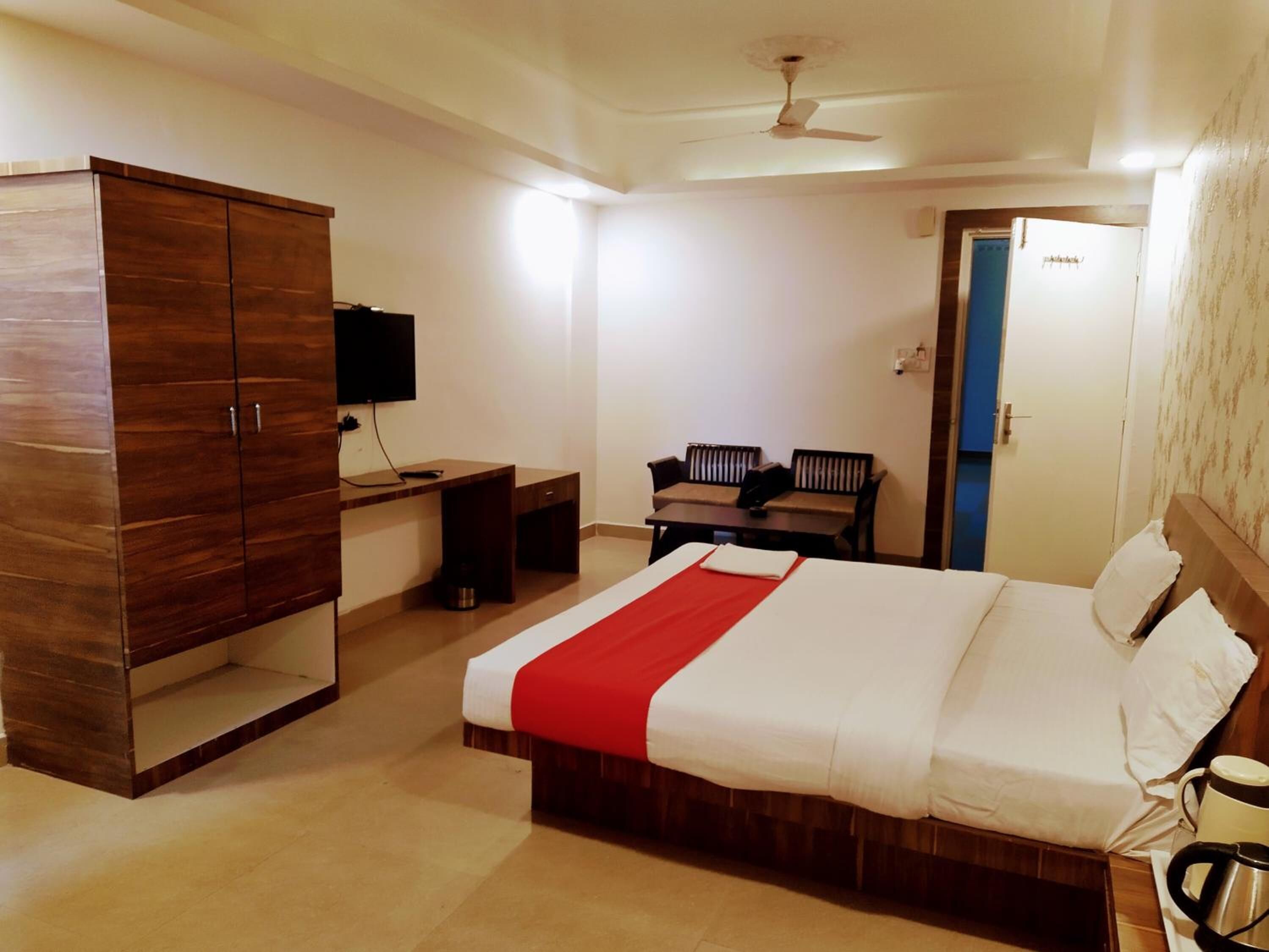 A hotel room with a bed, a wardrobe, a desk, a chair, a television, and a ceiling fan.