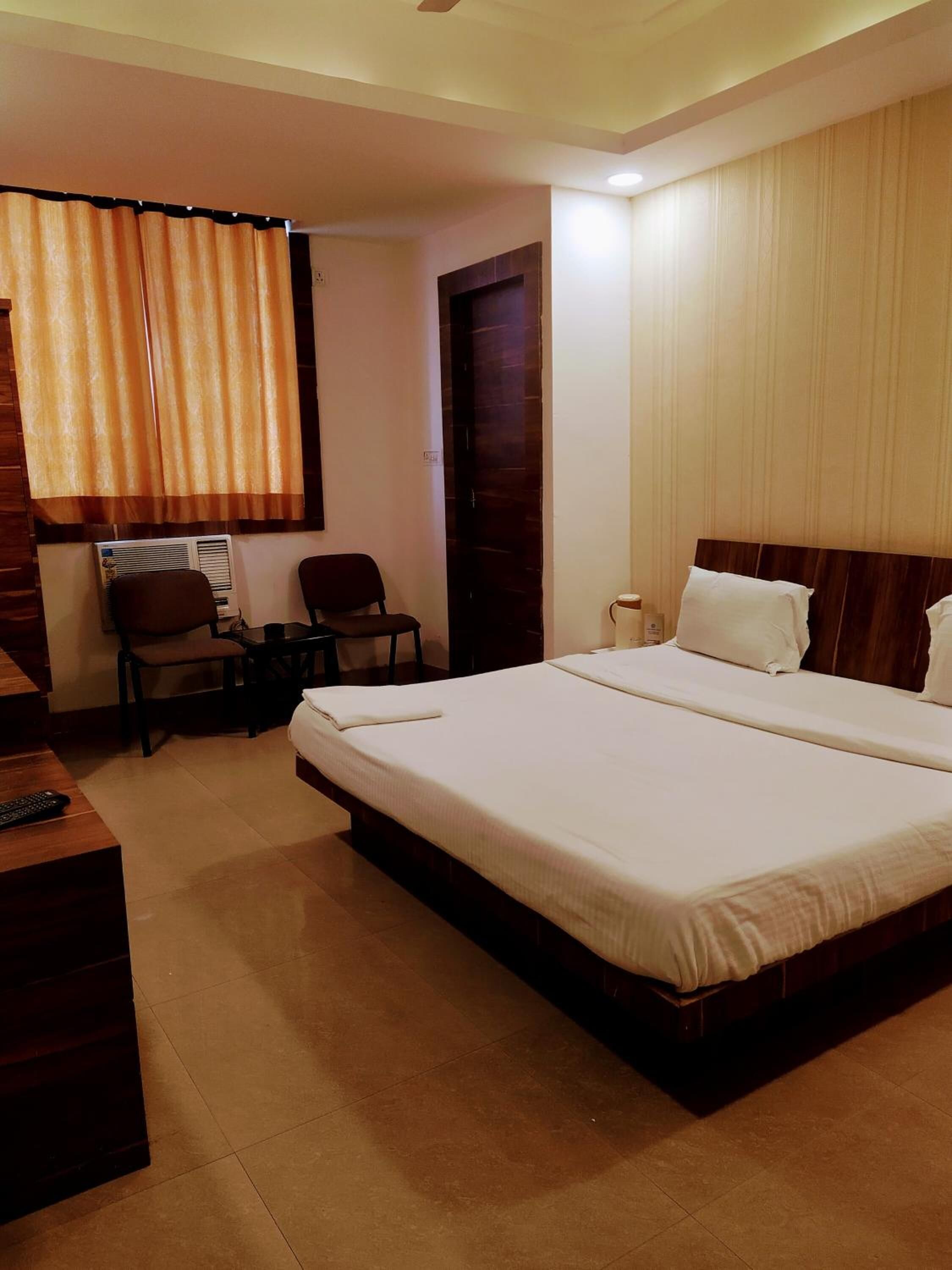 Une chambre d’hôtel avec un grand lit, un bureau avec une chaise, une petite table et une fenêtre avec des rideaux.