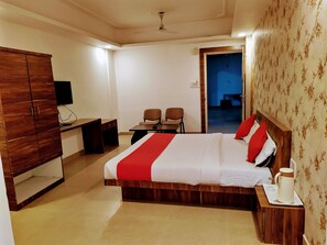 A hotel room with a large bed, a wooden wardrobe, a desk with a chair, and a television.