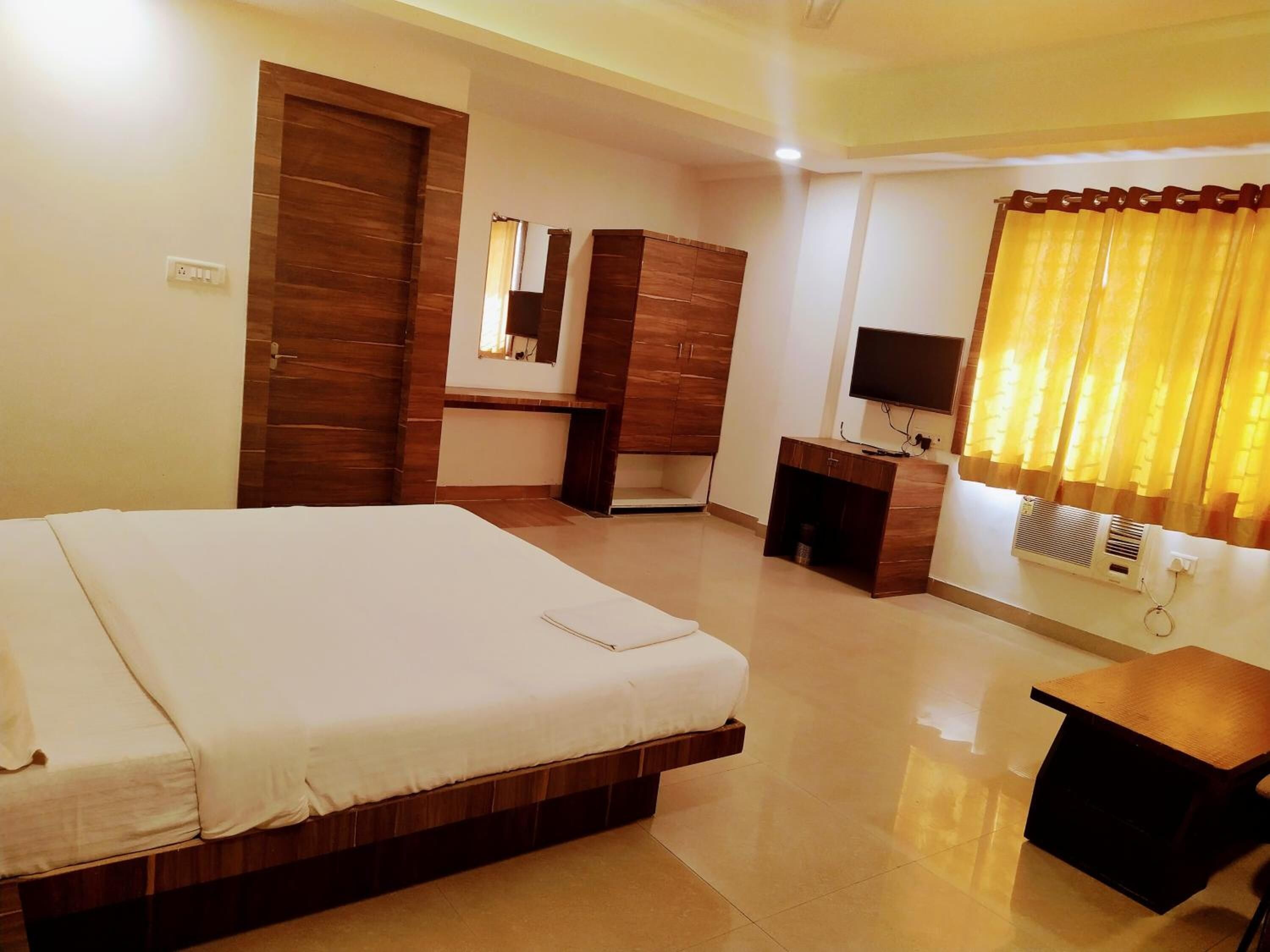 A hotel room with a bed, a desk, a TV, and a window with curtains.