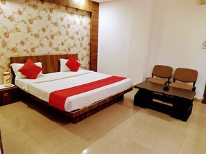 A hotel room with a wooden bed, two red pillows, a white bedspread, a red blanket, a wooden nightstand, a coffee maker, and a small table with two chairs.