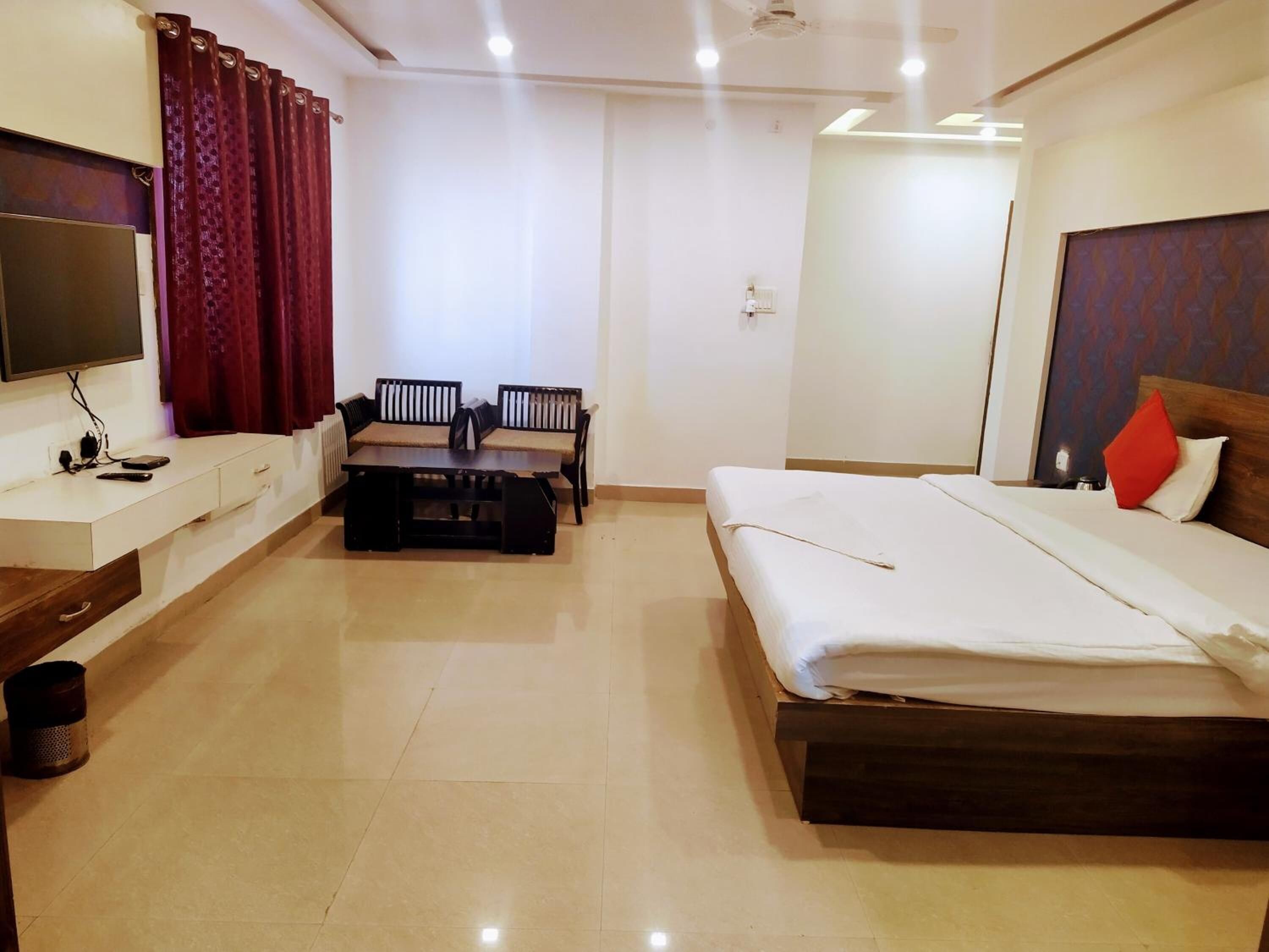 A hotel room with a bed, a desk, a chair, a TV, and a window with curtains.