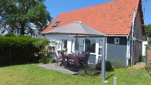 Ein Haus mit rotem Ziegeldach, einer Terrasse mit Tisch und Stühlen und einem Garten.