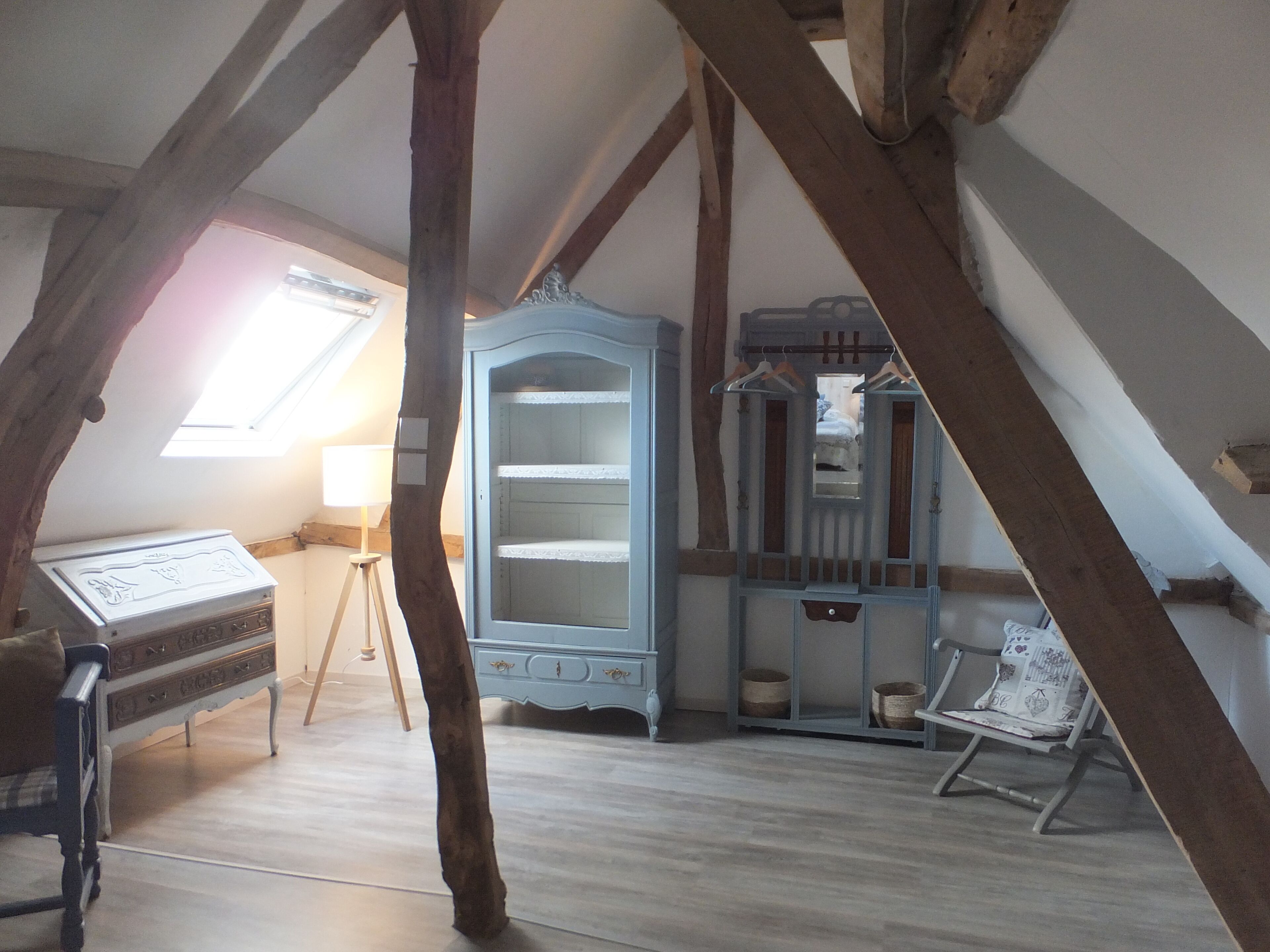 A room with exposed wooden beams, a blue cabinet with shelves, a piano, and a chair.