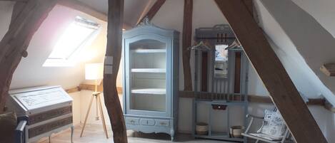 A room with exposed wooden beams, a blue cabinet with shelves, a piano, and a chair.