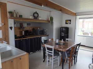 Una cocina con encimera de madera, un refrigerador negro, una mesa de comedor con sillas y un ventanal con vistas al exterior.