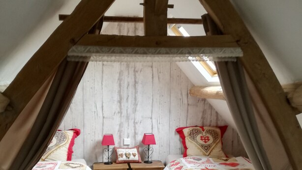 Ein gemütliches Schlafzimmer im Dachgeschoss mit zwei Betten, Holzbalken, einer weißen Wand und einem kleinen Fenster.