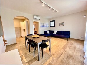 A modern living room with a dining area, a sofa, and an air conditioning unit.