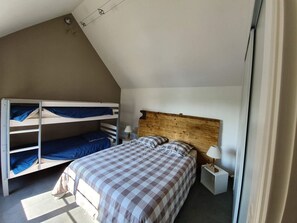 A dorm-style room with bunk beds, a wooden headboard, a bedside table with a lamp, and a checkered bedspread.
