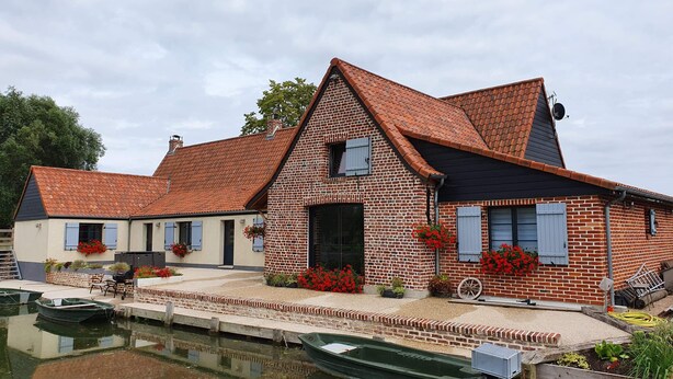 A traditional brick house with a tiled roof, a pond, and boats.