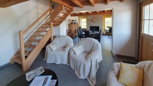 A spacious living area with a wooden staircase, a dining table with chairs, and a sofa.