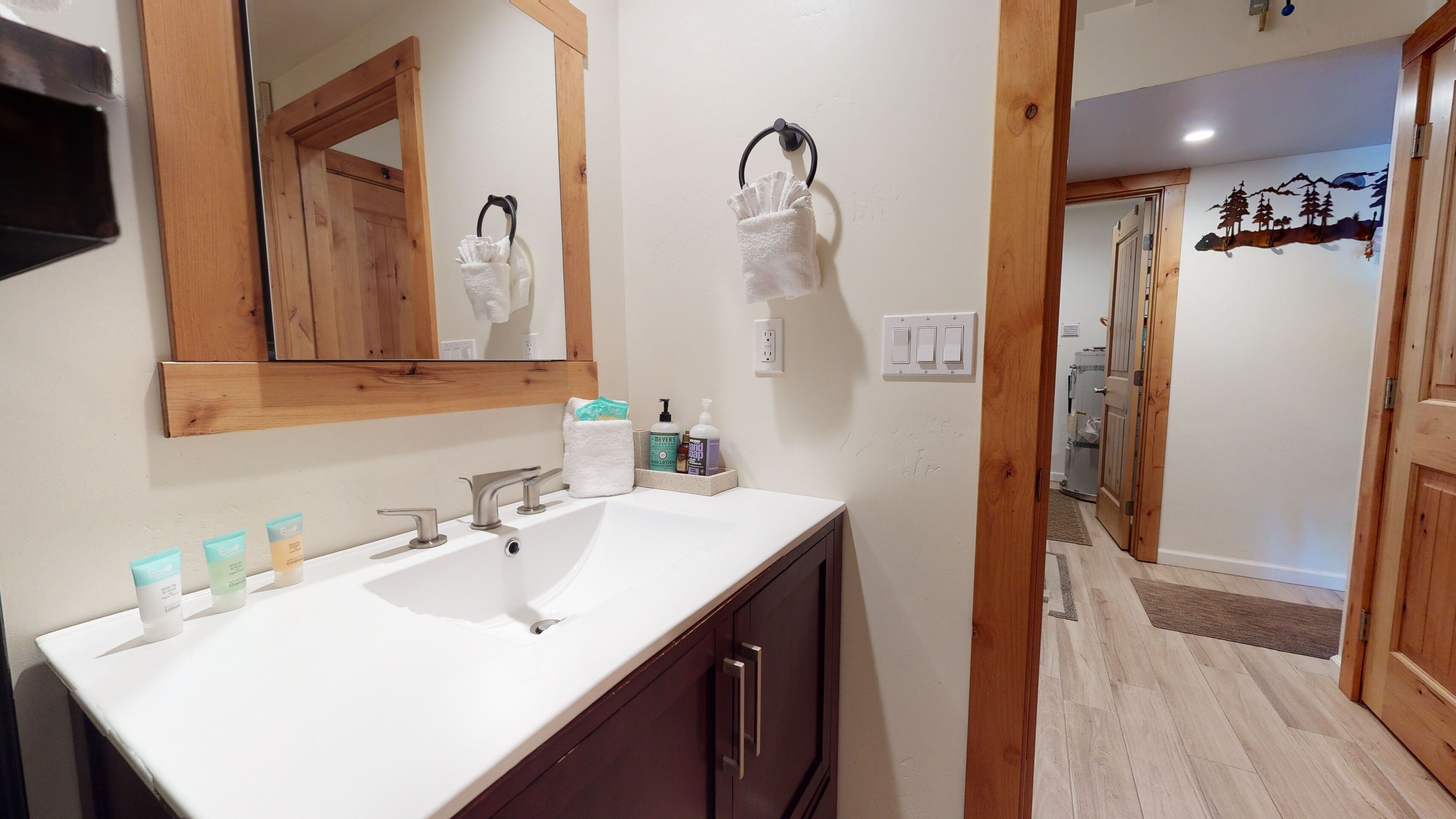 A bathroom with a white sink, two faucets, a mirror, and a towel rack. There are toiletries on the counter.