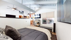 A modern bedroom with a large bed, a ceiling fan, a TV, and a view of the outdoors. - Mammoth Estates Studio Condos - 2 Blocks from The Village Gondola Station by RedAwning (Mammoth Lakes)