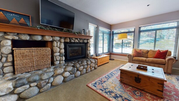 A living room with a stone fireplace, a television mounted above it, a sofa with cushions, and a patterned rug. - Silver Bear #30 2 Bedroom Condo (Mammoth Lakes)
