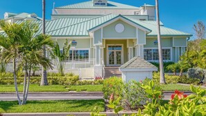 A two-story building with a green roof and white trim, surrounded by well-maintained landscaping including palm trees and flowering plants.