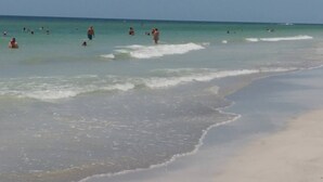 A beach with people swimming and walking along the shore.
