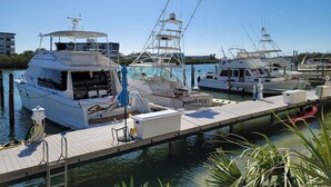 A marina with several yachts docked, featuring a wooden dock and clear skies.