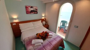 Un lit bien fait, recouvert d’une courtepointe violette, un bouquet de fleurs et un tableau accroché au mur.