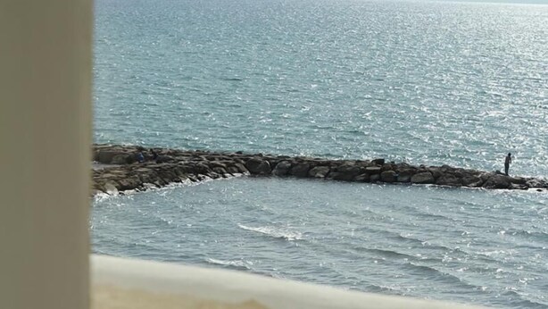 Un balcon avec vue sur la mer, une table ronde et un mur en pierre.