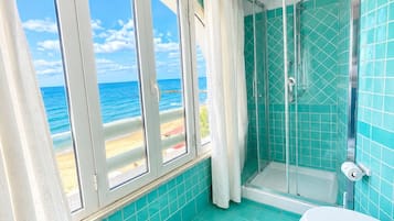 A bathroom with a glass shower, a toilet, and a window with a view of the beach.