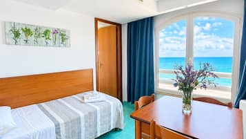 A room with a bed, a table, and a view of the sea.