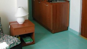 A compact kitchen with wooden cabinets, a small countertop, and a sink. There is a nightstand with a lamp and a book. - Two-room apartment, beachfront, floor 2 (Sunflower) (Anzio)