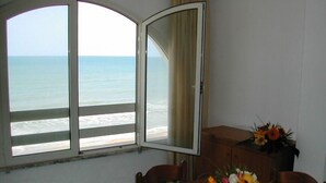 A room with a large window overlooking the sea, a wooden table with a floral centerpiece, and a wooden cabinet. - Two-room apartment, beachfront, floor 2 (Sunflower) (Anzio)