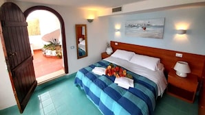 Quarto com cabeceira de madeira, cama com roupa de cama azul e branca, mesa de cabeceira com abajur, espelho e pintura na parede.