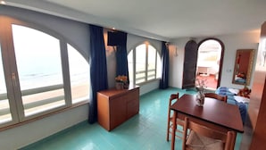 Um quarto com janelas amplas, uma escrivaninha de madeira, uma mesa de jantar e uma cama.