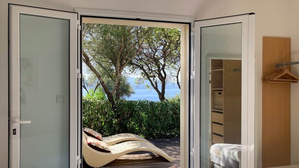 Une chambre dotée d’une porte-fenêtre coulissante donnant sur un balcon avec vue sur la mer et les arbres.