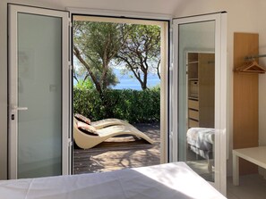 Quarto com porta de correr de vidro que dá para uma varanda com vista para o mar e árvores.