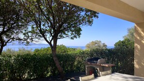 Une terrasse extérieure avec une table et des chaises, offrant une vue panoramique sur la mer et les collines.