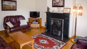 A living room with a fireplace, leather sofas, a wooden coffee table, and a television. - Boherbue Holiday Home (Boherboy)