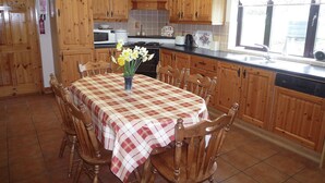 A kitchen with wooden cabinets, a dining table with a checkered tablecloth, and a vase of flowers. - Boherbue Holiday Home (Boherboy)