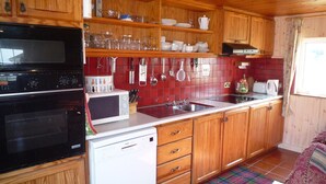 Une cuisine compacte avec des meubles en bois, un four à micro-ondes, un lave-vaisselle et un dosseret de carrelage rouge.